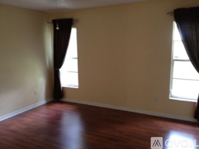 A room with wooden floors and two windows with curtains.