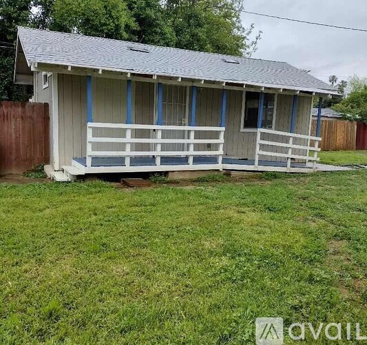A small house with a porch and a fence in the yard.