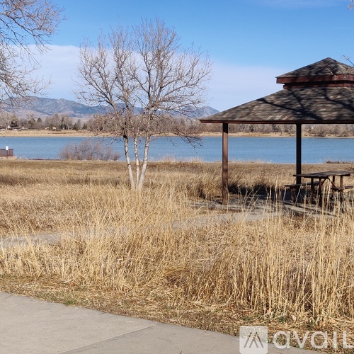 A wooden gazebo sits in a field by a lake.