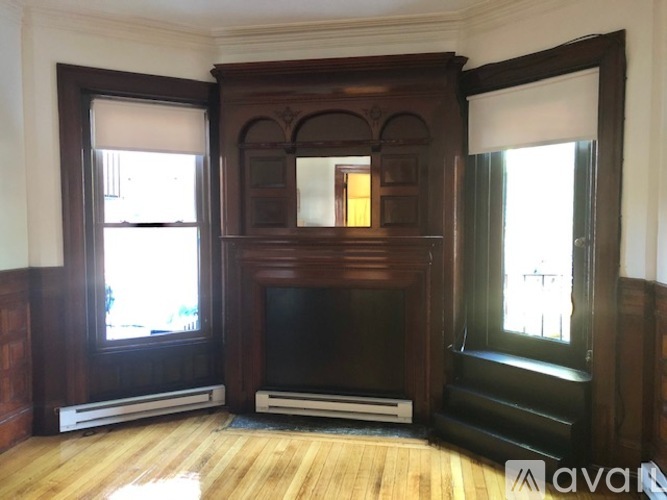 A large wooden fireplace with a TV above it in a room with wooden floors and white walls.