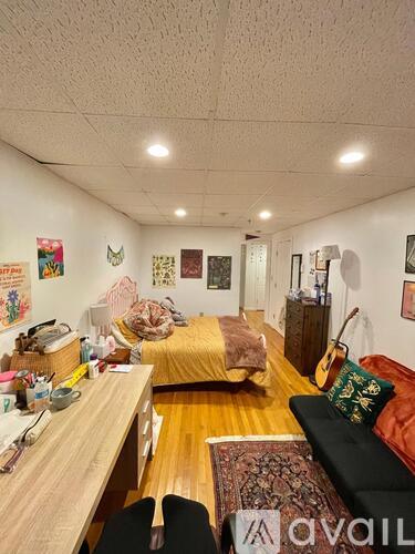 A room with a bed, a couch, a desk, and a guitar.