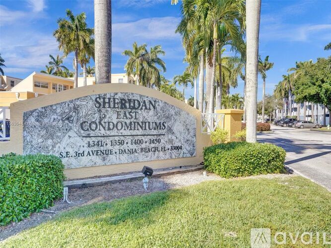 A sign for Sheridan East Condominiums stands in front of a row of palm trees.