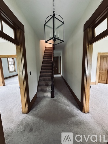 A large, empty room with a staircase and a hanging light fixture.