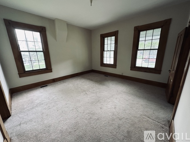 A room with carpeted floor and three windows.