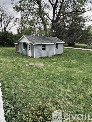 A small house with a white door and a grey roof is surrounded by a grassy area.