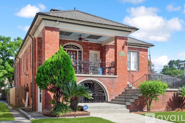 A red brick house with a balcony and a tree in front.