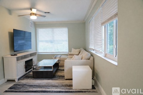 A living room with a white couch, a black coffee table, and a television on a cabinet.