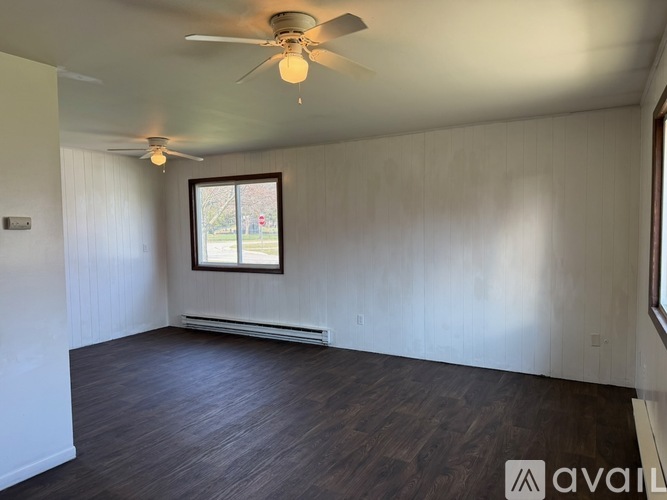 A room with a ceiling fan and a window showing a view of a tree and a fence.
