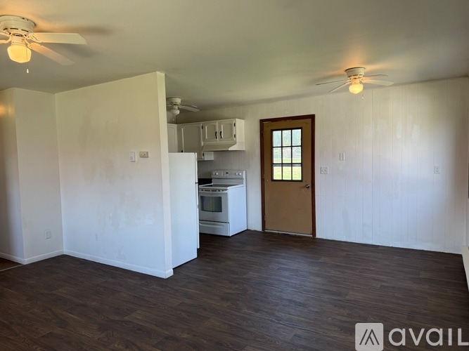 A room with a wooden door and a kitchen in the background.