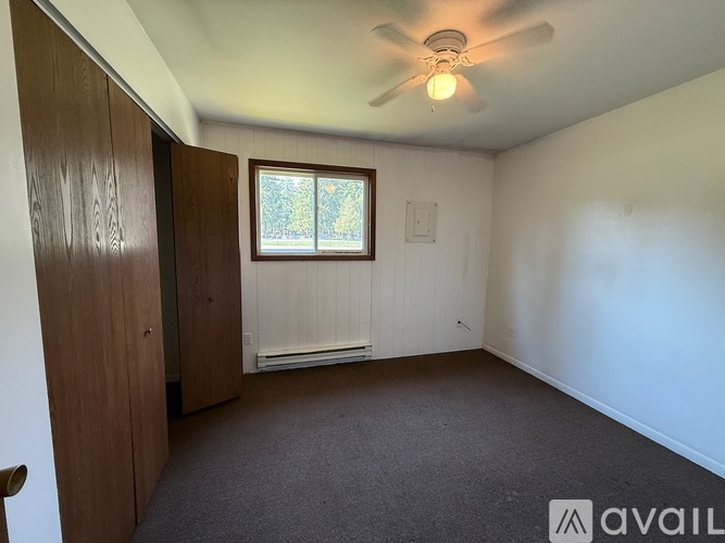 A room with a ceiling fan and a window with a view of trees.