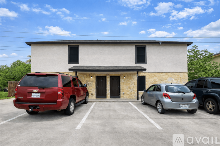 A red SUV is parked in a parking lot in front of a building with a stone facade and a black door.