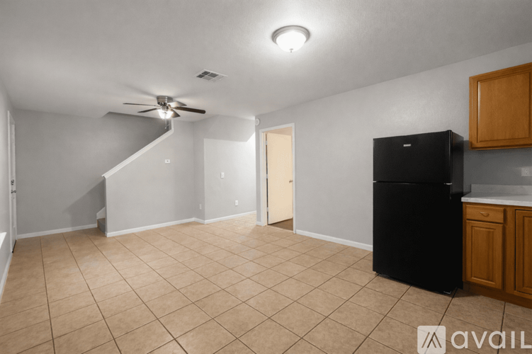 A kitchen area with a black fridge, wooden cabinets, and a ceiling fan.