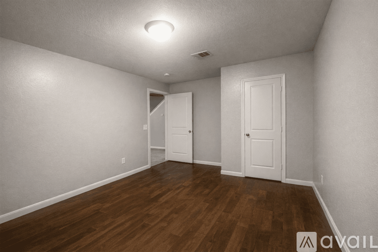 A room with wooden floors and white walls, with two doors and a ceiling light.
