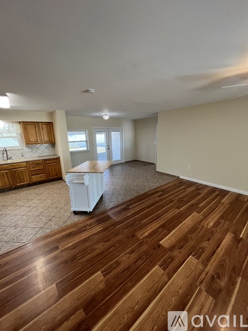 A room with wooden flooring and a kitchen area in the background.