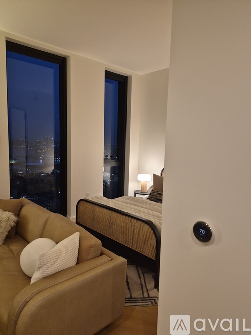 A bedroom with a bed, couch, and a window overlooking a cityscape.