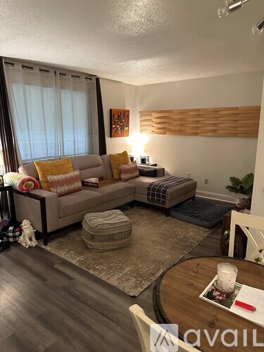 A living room with a couch, ottoman, and a table with a candle on it.
