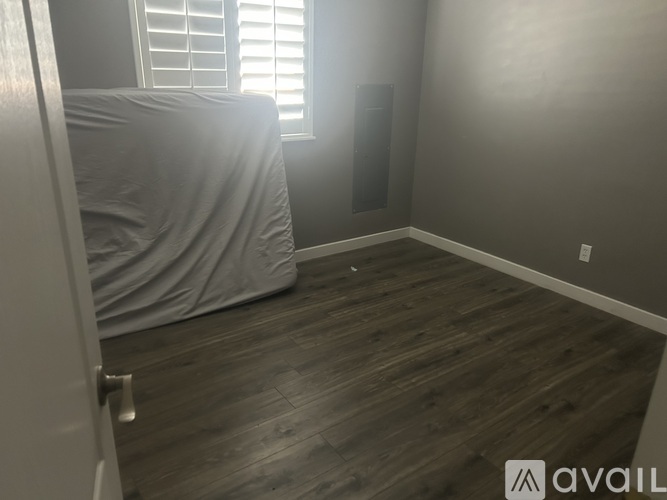 A room with a bed covered in a white sheet and wooden flooring.