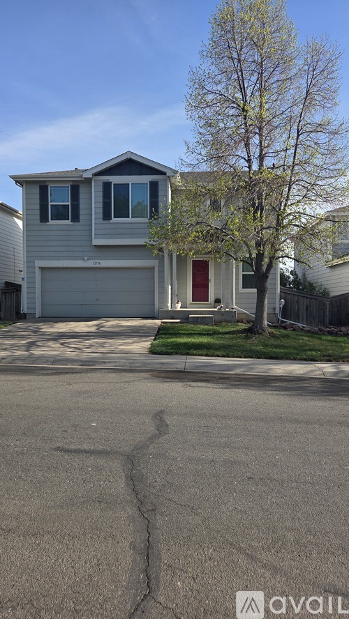 A house with a grey exterior and a red door is situated in front of a tree.