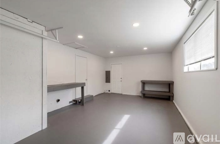 A spacious room with a grey floor and white walls, equipped with a built-in bench and a window.