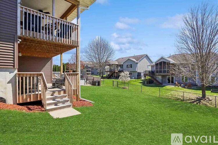 A balcony with a staircase leading to a grassy area with houses in the background.