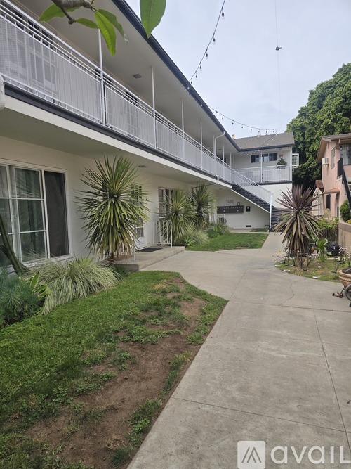 A white building with a balcony and plants in front.
