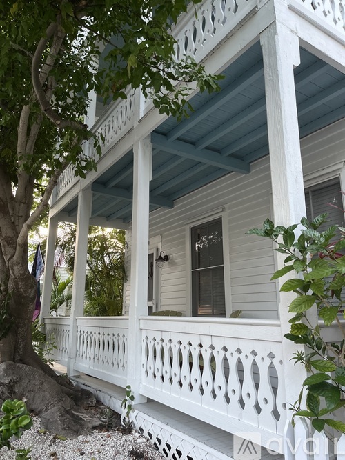 A white porch with a blue roof and a tree in front.