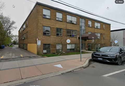 A black car is parked on the side of a street in front of a brick building.