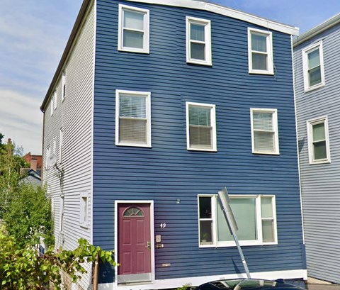 A blue house with a red door and a ladder leaning against it.
