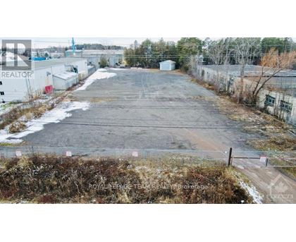 A large, empty parking lot with a fence and some buildings in the background.