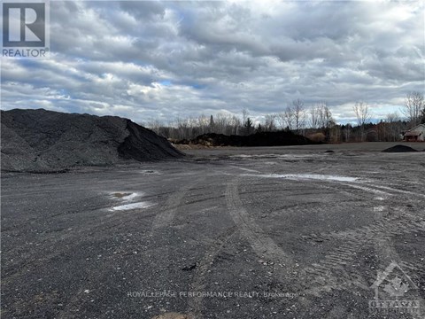 A large open area with tire tracks in the foreground and a pile of dirt in the background.