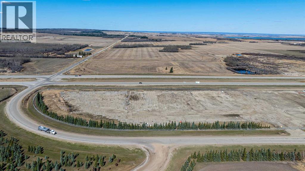 A large open field with a road curving around it and a car driving on the road.