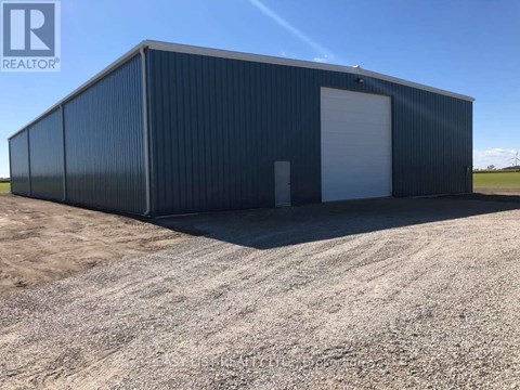 A large black building with a white door is situated on a gravel lot.