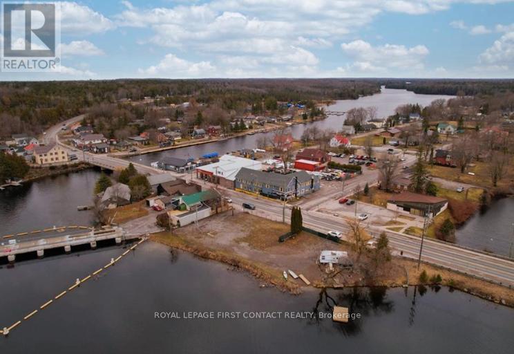 A real estate company logo is superimposed on an aerial view of a small town by a lake.