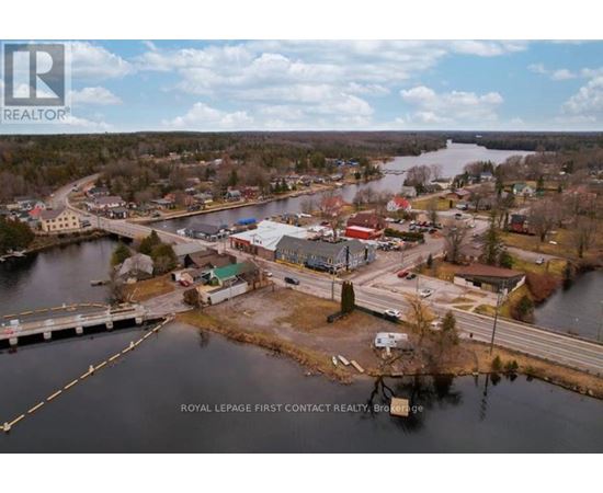 A real estate company logo is superimposed on an aerial view of a small town by a lake.