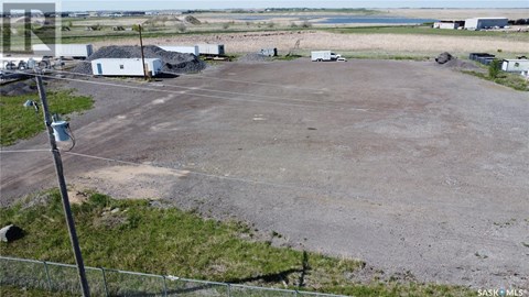 A large, empty parking lot with a fence and a few buildings in the background.