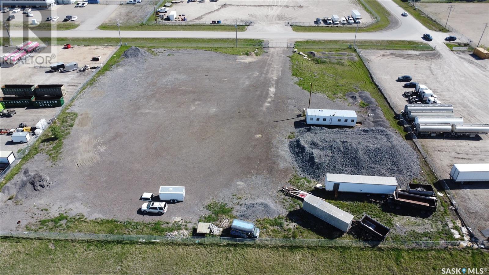 An aerial view of a construction site with a large open area in the center and various buildings and vehicles surrounding it.
