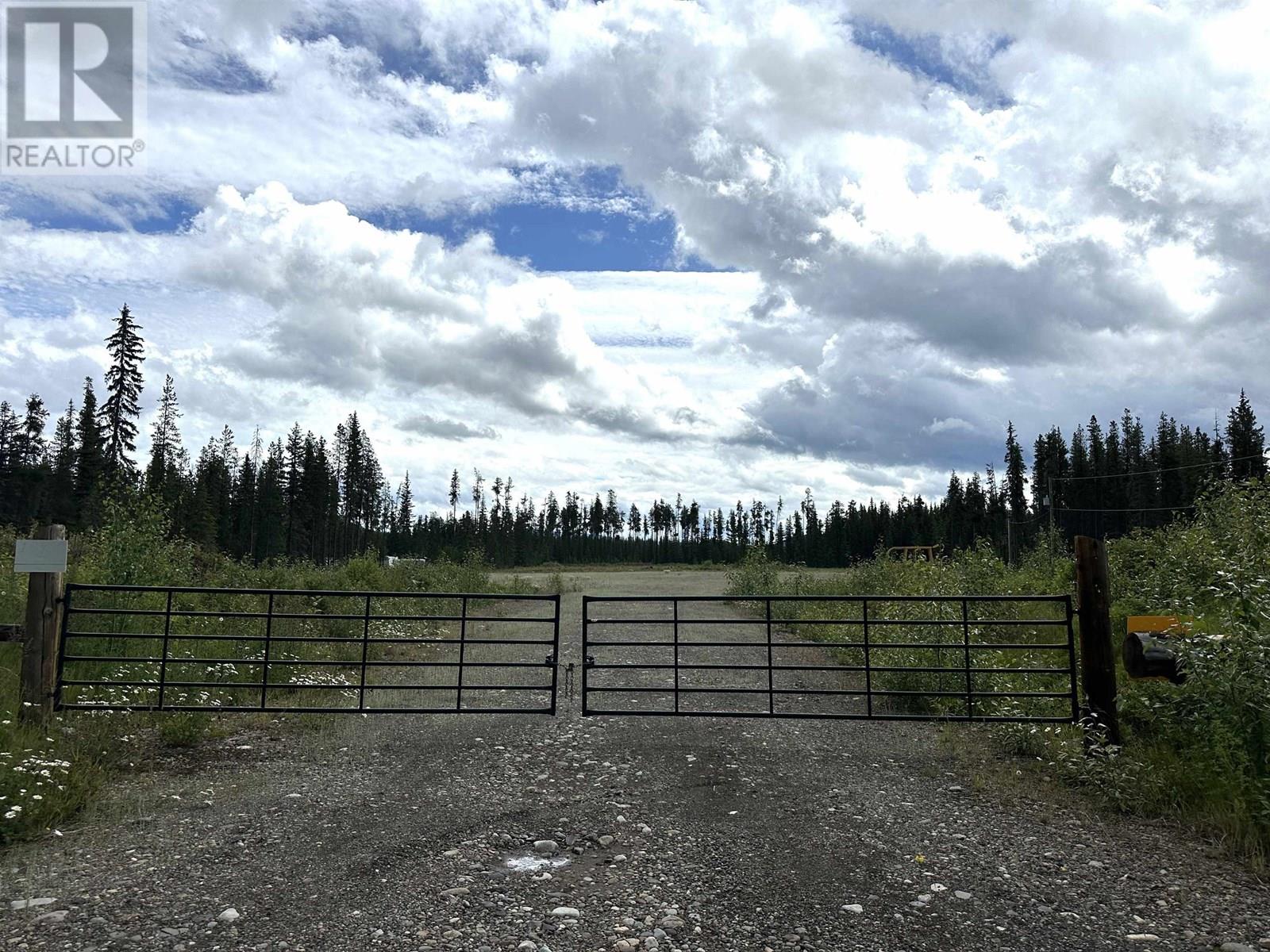 A gate with a sign that says REALTOR in front of a forest.