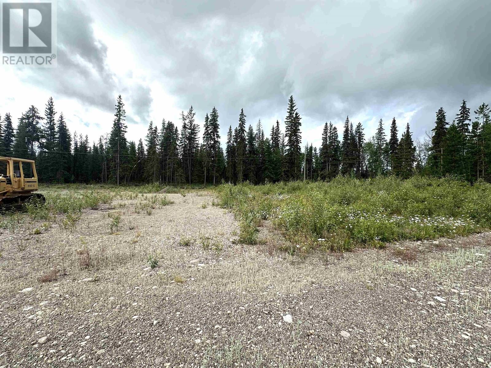 A barren land with a forest in the background and a bulldozer on the left side.