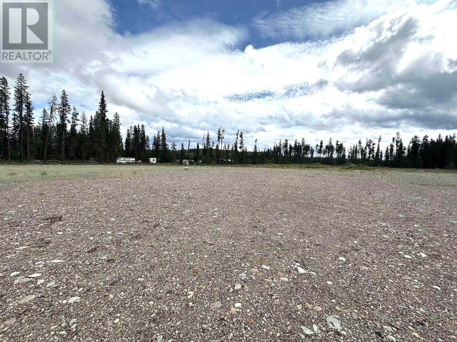 A gravel field with trees and a cloudy sky.