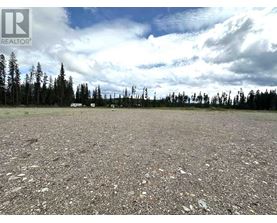 A gravel field with trees and a cloudy sky.