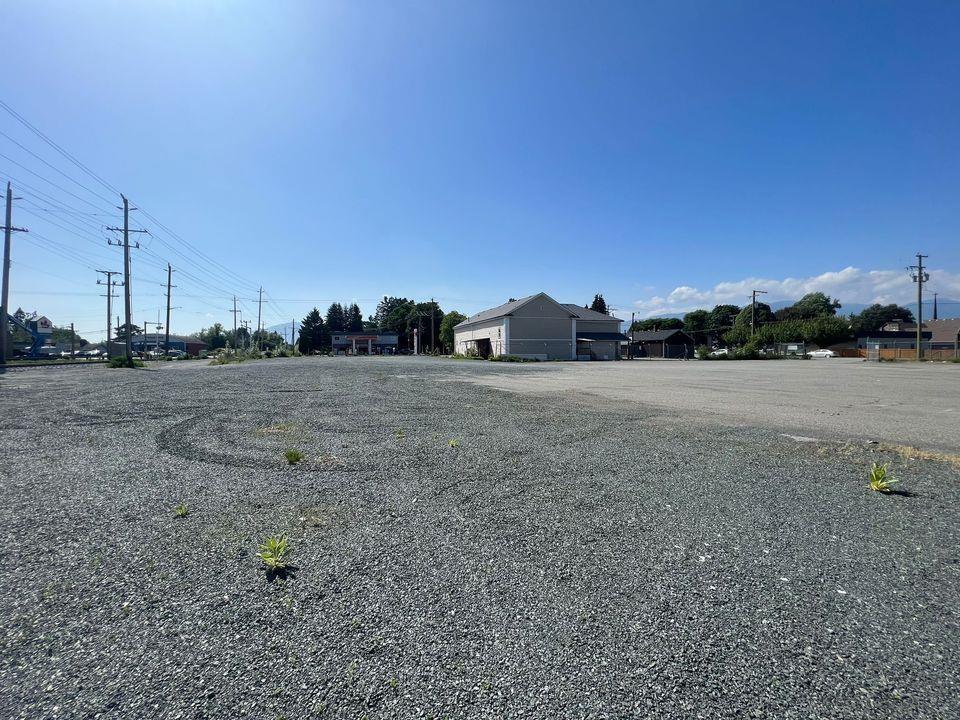 A gravel parking lot with a building and power lines in the background.