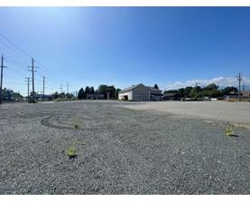 A gravel parking lot with a building and power lines in the background.