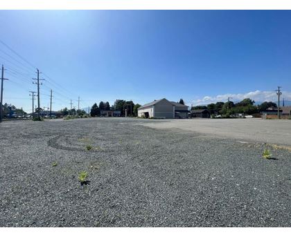 A gravel parking lot with a building and power lines in the background.