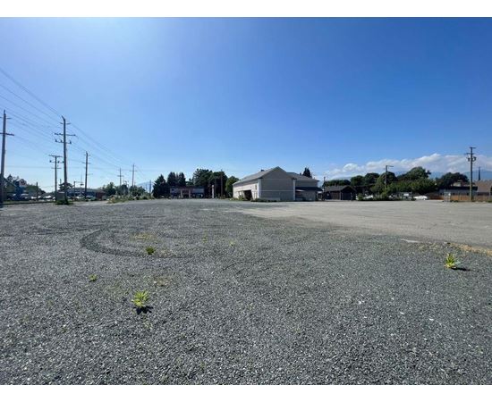 A gravel parking lot with a building and power lines in the background.