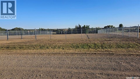 A large, empty field with a fence and trees in the distance.