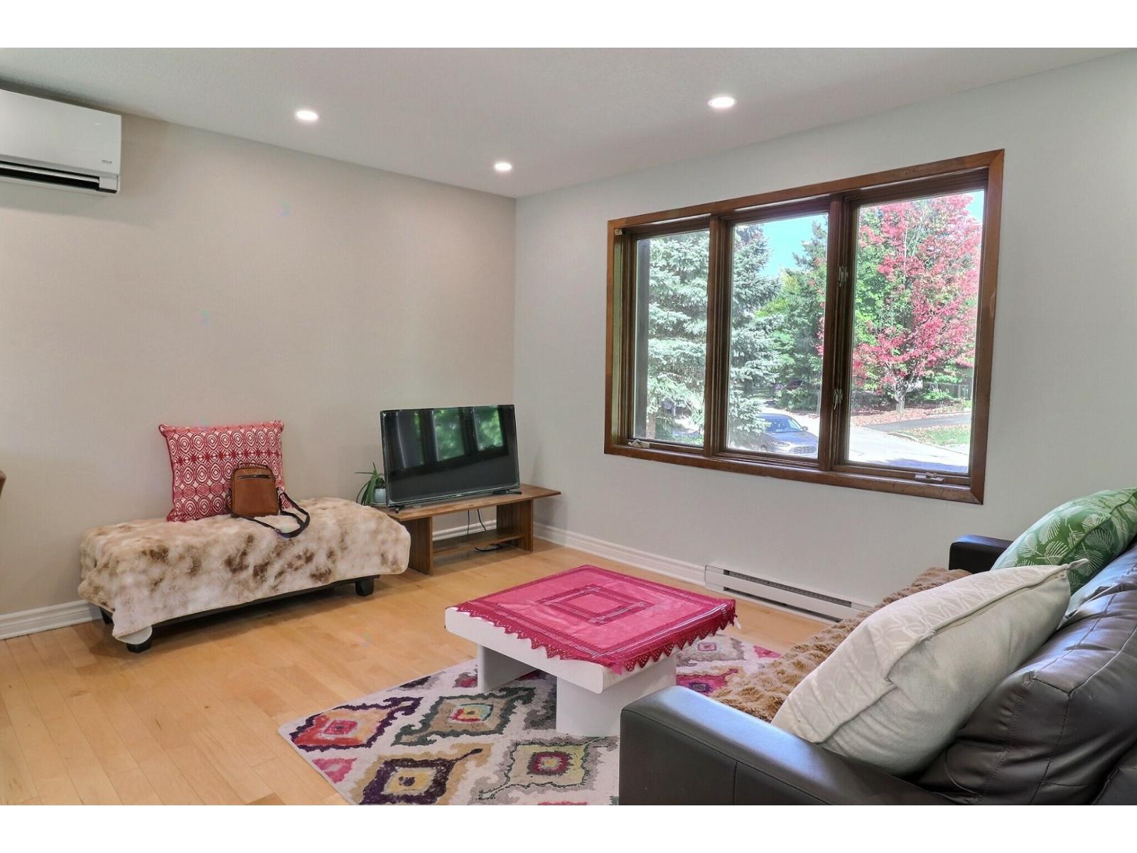 A living room with a grey couch, a pink ottoman, and a television.