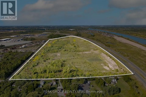 An aerial view of a property with a white boundary line, surrounded by greenery and a river in the distance, with the Peak Group Realty logo and address in the corner.