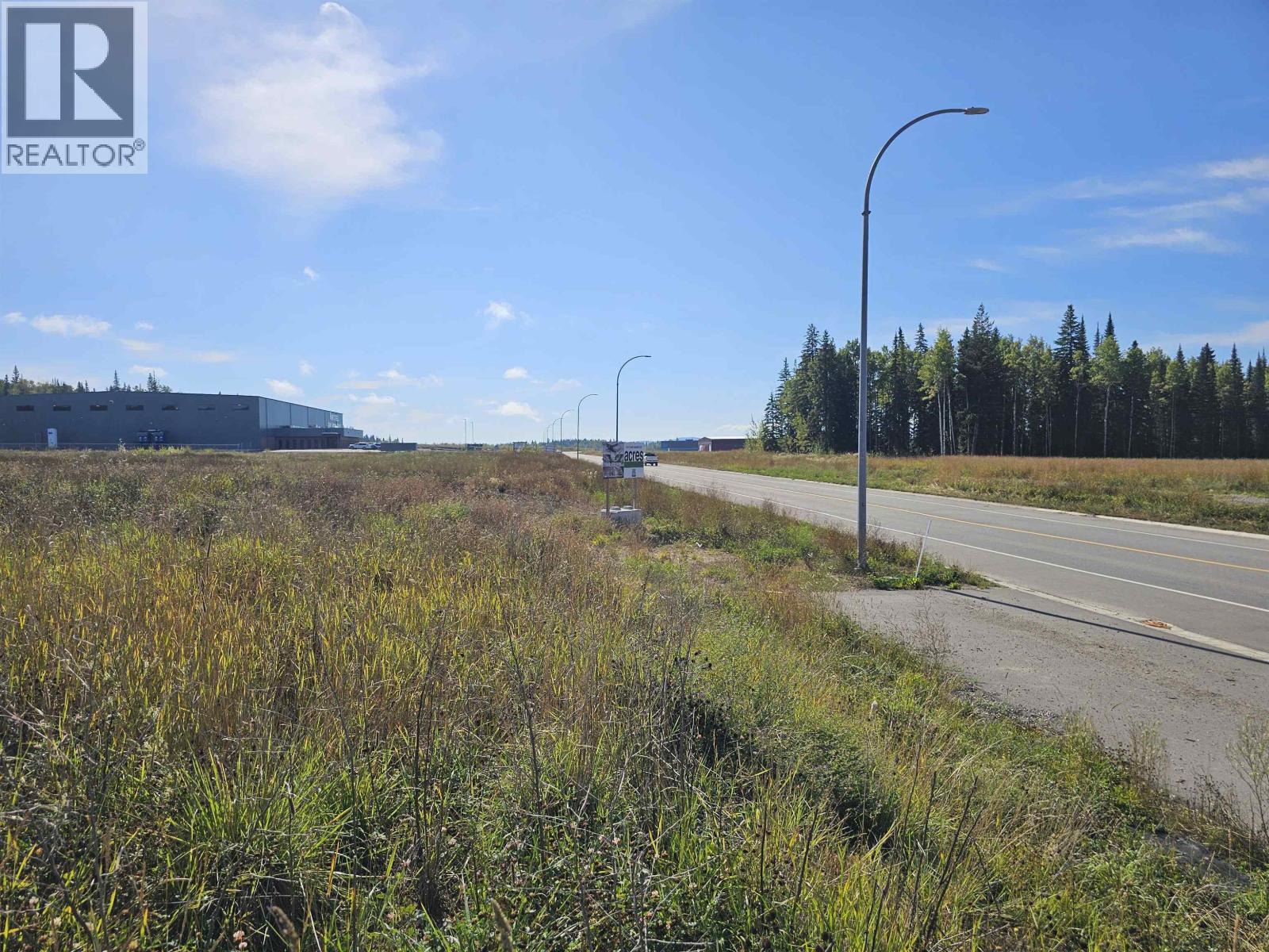 A road with a grassy area on the side and a building in the distance.