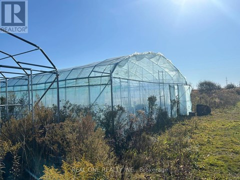 A large greenhouse with a transparent roof and walls is surrounded by greenery and trees.