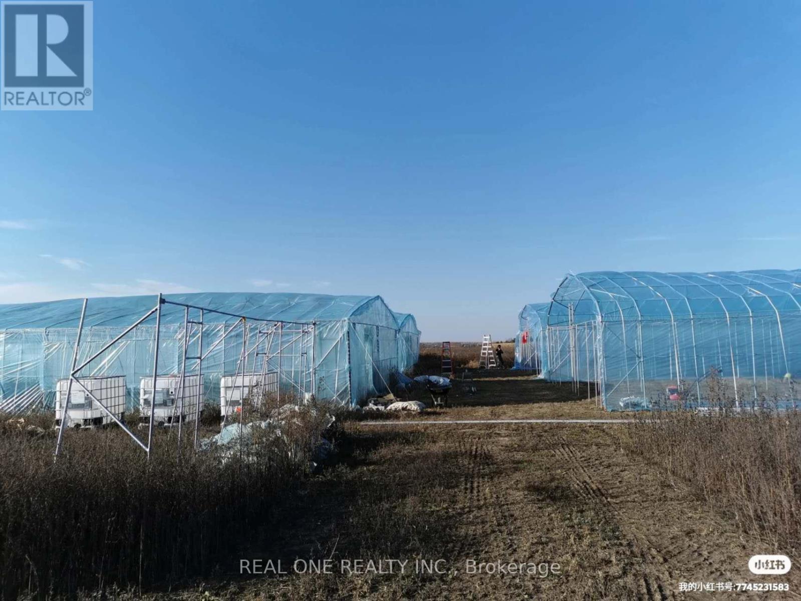 A field with a greenhouse and a REALTOR sign.